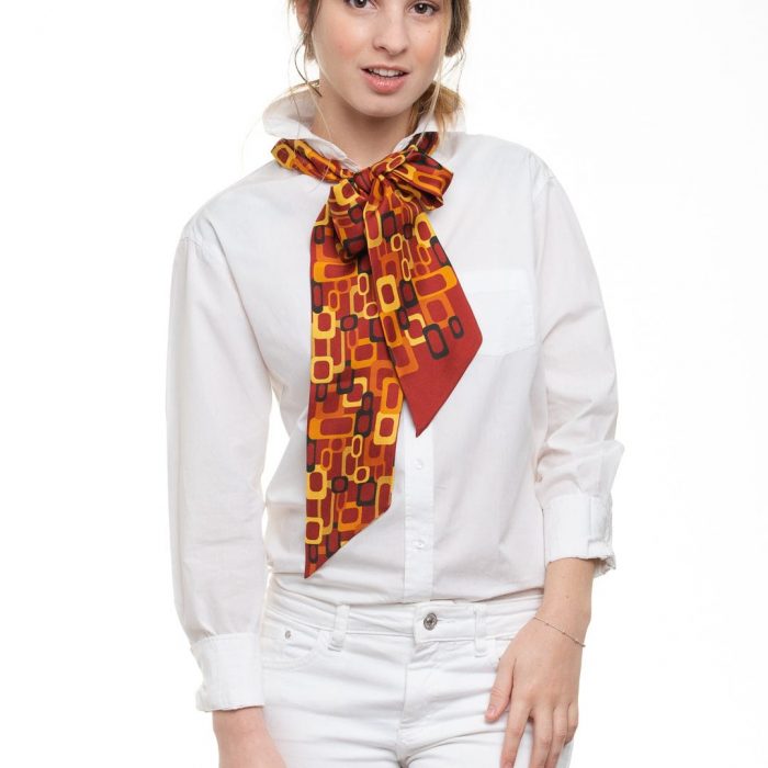Model wearing the versatile Links twilly around the neck, emphasizing the bright red background against the outfit. Essential accessory for all seasons.