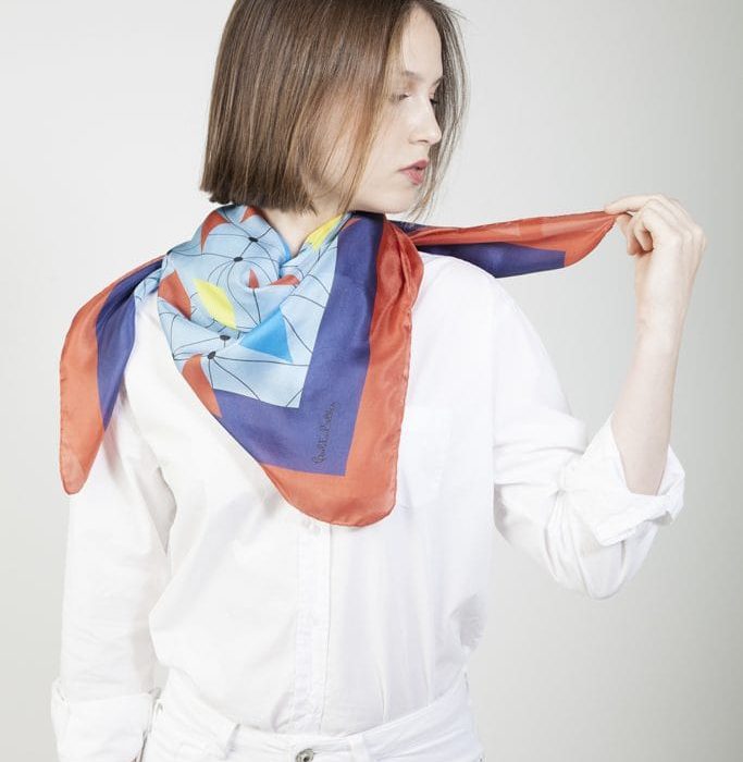 Model wearing the 'Flying Macaws' silk scarf styled as a sash, highlighting the dynamic flow of the connected triangles pattern.